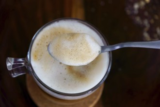 Creamy coffee foam being lifted by a spoon from a glass cup, creating a close-up view of the rich