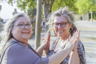Two happy senior women are giving high five in a park, celebrating friendship and active lifestyle
