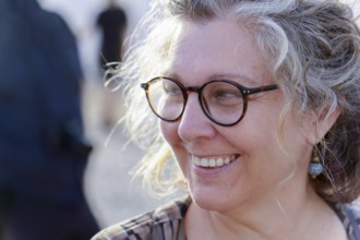 Close-up of cheerful mature woman with eyeglasses, enjoying golden hour sunlight, showcasing a