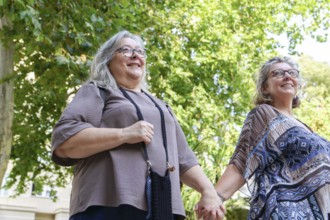 Two happy senior women holding hands and walking in a park, enjoying a sunny day together