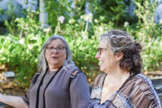 Two happy middle-aged women enjoying a conversation in a botanical garden, surrounded by lush