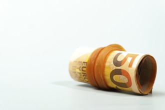 Rolled 50 euro banknotes secured by an orange rubber band lying on a white background represent