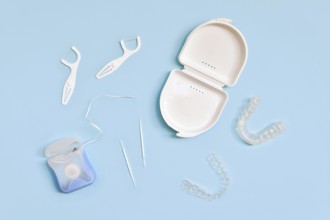 Top view of dental clear aligners, case, toothpicks and floss on blue background