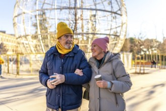Smiling senior couple walking arm in arm in a winter city park with a large christmas decoration