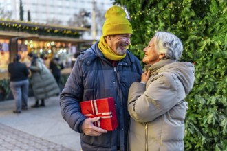 Loving senior couple exchanging christmas gifts at a festive outdoor market, enjoying the holiday