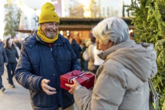 Happy senior man presenting a christmas gift to his wife while enjoying the festive atmosphere of a