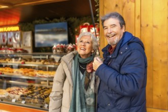 Cheerful senior couple enjoying christmas market, shopping and having fun during winter holidays