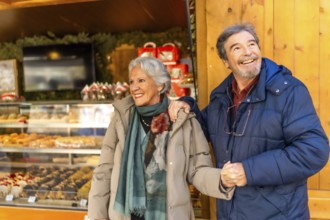 Smiling senior couple holding hands and visiting a traditional christmas market, enjoying winter