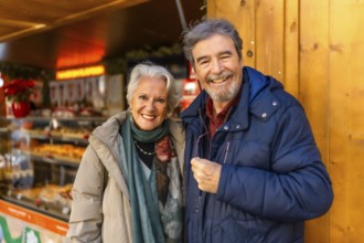 Cheerful retired couple enjoying christmas market during winter holidays, buying presents and
