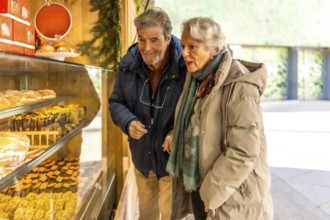 Happy retired couple selecting delicious sweets and cakes at a charming wooden stall in a festive
