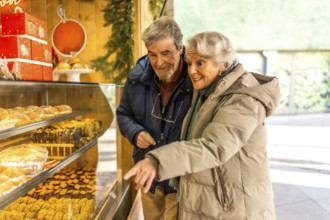 Happy senior couple pointing and choosing delicious pastries from a display at an outdoor christmas
