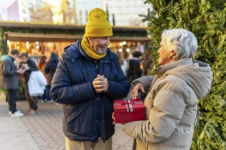 Elderly man and woman exchanging gifts at a christmas market in the city during winter holidays