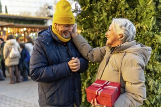 Loving senior couple exchanging christmas gifts at a traditional christmas market, enjoying festive