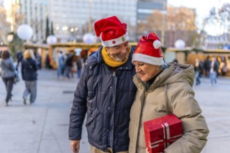 Smiling senior couple wearing santa hats holding hands and enjoying christmas market in the city