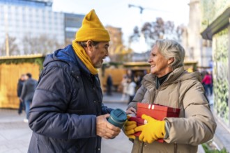 Happy senior couple exchanging christmas gifts and enjoying a warm beverage at a bustling outdoor