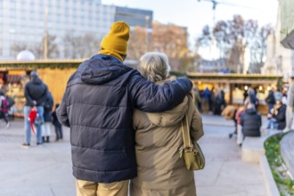 Elderly couple hugging at outdoor christmas market in european city during winter holidays