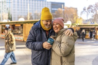 Elderly couple sharing warm drinks while enjoying the festive atmosphere of an outdoor christmas