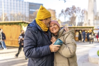 Affectionate senior couple enjoys warm drinks at a christmas market in a winter city setting