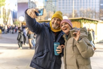 Smiling senior couple taking selfie with smartphone while enjoying hot drinks at a christmas market