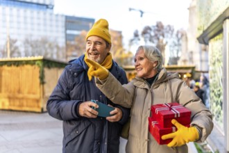 Cheerful senior couple holding christmas gifts and pointing at something interesting at the