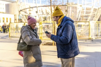 Elderly couple enjoying christmas time in a winter city, sharing a moment of joy with a smartphone