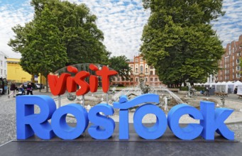 Vist Rostock logo, behind it fountain of joie de vivre, behind it university, university square,