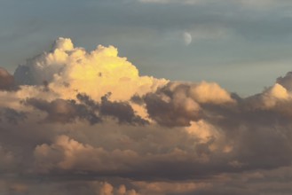 Cumulus cluster clouds are bathed in warm light as dusk falls, illuminated in the background at the