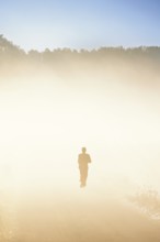 Alone person in silhouette running on a dirt road in the countryside in the morning fog