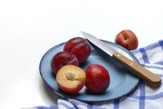 Red plums on plate with kitchen knife, Prunus domestica