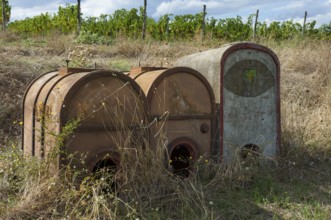 Rusted containers, mobile tanks for water or pesticides in front of vineyards
