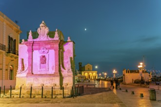 The colourfully illuminated Greek fountain Fontana Greca at dusk, Gallipoli, Apulia, Italy