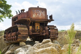 Old, heavily rusted bulldozer for road construction stands abandoned on rocks, industrial relic