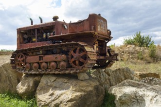 Old, heavily rusted bulldozer for road construction stands abandoned on rocks, industrial relic