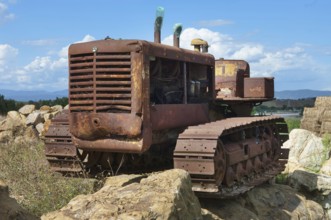 Old, heavily rusted bulldozer for road construction stands abandoned on rocks, industrial relic