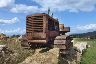 Old, heavily rusted bulldozer for road construction stands abandoned on rocks, industrial relic