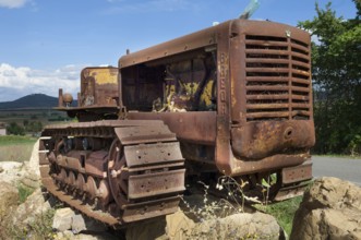 Old, heavily rusted bulldozer for road construction stands abandoned on rocks, industrial relic