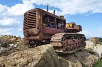 Old, heavily rusted bulldozer for road construction stands abandoned on rocks, industrial relic