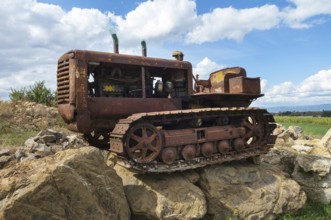 Old, heavily rusted bulldozer for road construction stands abandoned on rocks, industrial relic