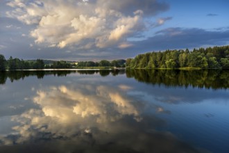 The Postfelden reservoir in the evening at the golden hour. Glowing clouds are reflected in the