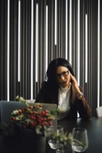 A businesswoman is seated at a desk in a contemporary office, deep in thought, with stylish