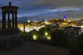Night view of Edinburgh with illuminated buildings and a historical monument in the foreground, Old