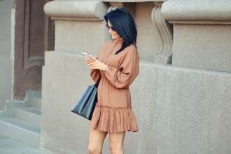 A cheerful woman stands on the street and watching as an online taxi ordered through a smartphone