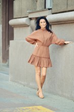A woman stands gracefully against a textured wall in a stylish dress. The urban setting features