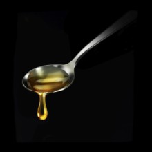 Honey drips from a spoon in front of a black background