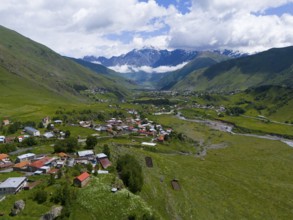 Village in a wide valley between green mountains with clouds in the sky, landscape near Kazbegi,