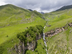 Landscape with long waterfall between green mountains under a cloudy sky, aerial view, Toti