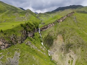 Waterfall cascading down the rocky mountain face, surrounded by green landscape, aerial view, Toti