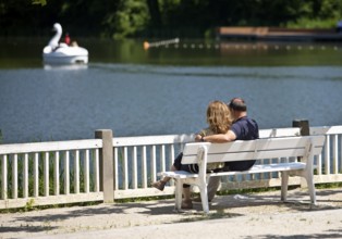 Couple sitting on a wooden bench and looking at the spa pond in the spa gardens, Großer Teich, Bad