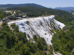 A limestone hillside overlooked by a wooded area under a blue sky, aerial view, Akkaya Travertines,