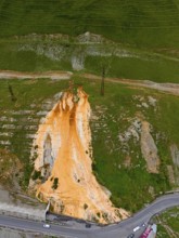 Aerial view of a hill with striking orange rock formation between roads and green landscape, aerial